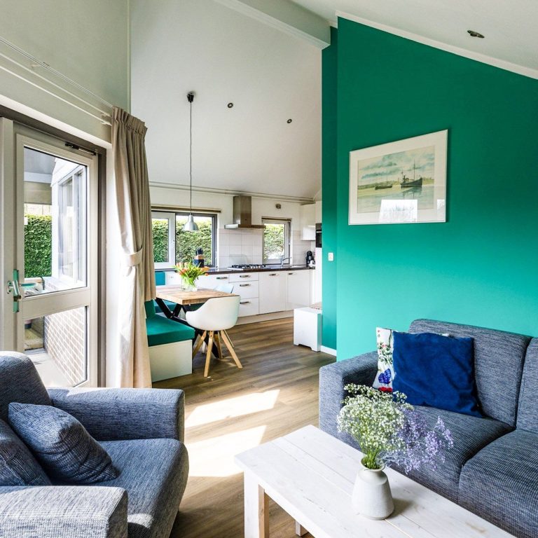 Moderne woonkamer met groene muur, donkere banken en een open keuken.