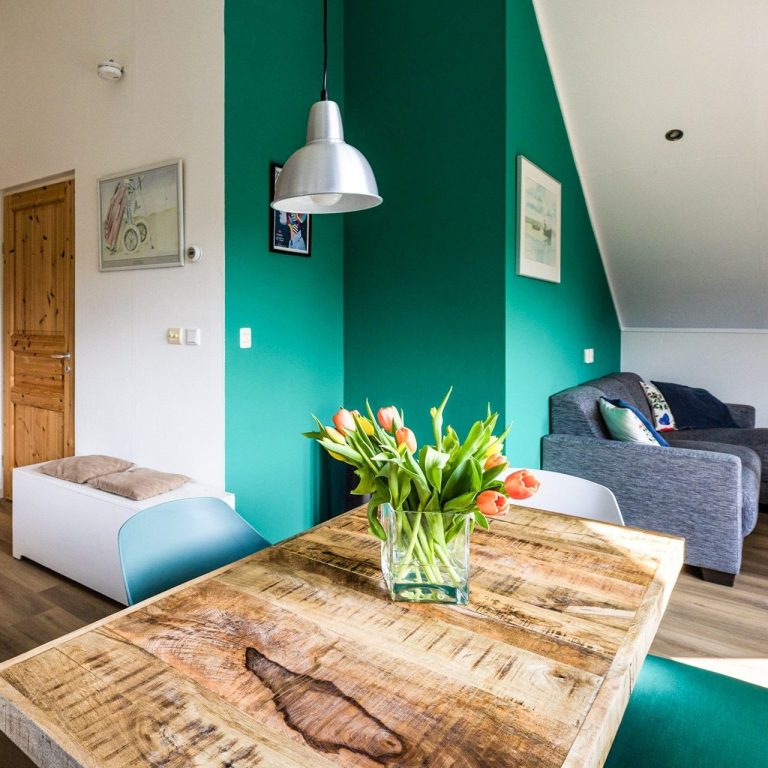 Eenvoudige woonkamer met groene muur, houten tafel en vaas met tulpen.