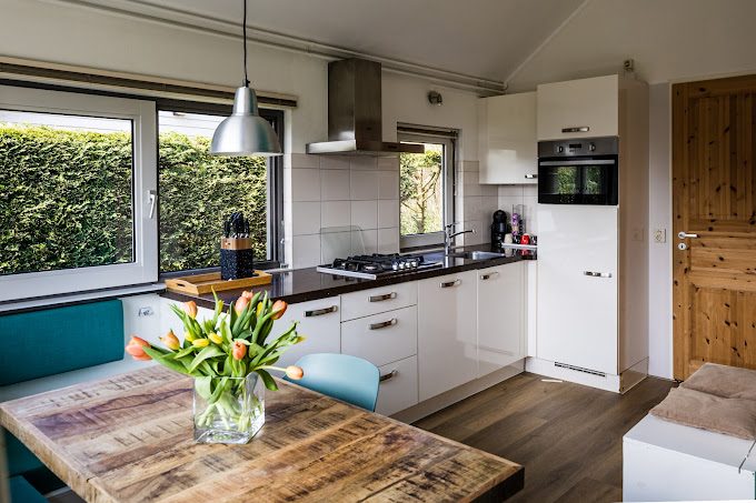 binnen in de Zeebungalow Moderne keuken met een houten tafel, bloemen, en apparaten in lichte kleuren.