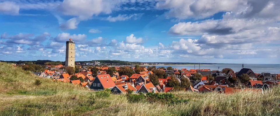 Terschelling en brandaris Panoramisch uitzicht op een dorp met rode daken en een toren, omringd door natuur en zee.