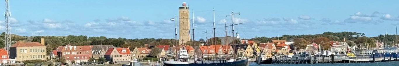 Terschelling bij aankomst Haven met boten en een toren, omgeven door kleurrijke gebouwen en bomen.