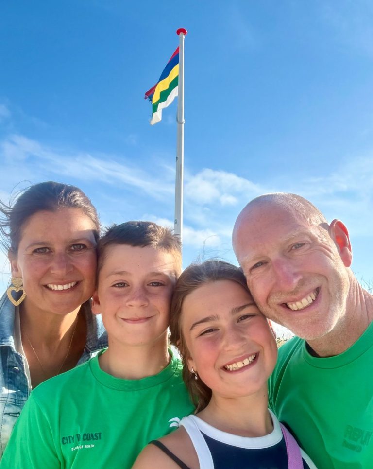 Gezin met vlag op de achtergrond, lachend onder een blauwe lucht.