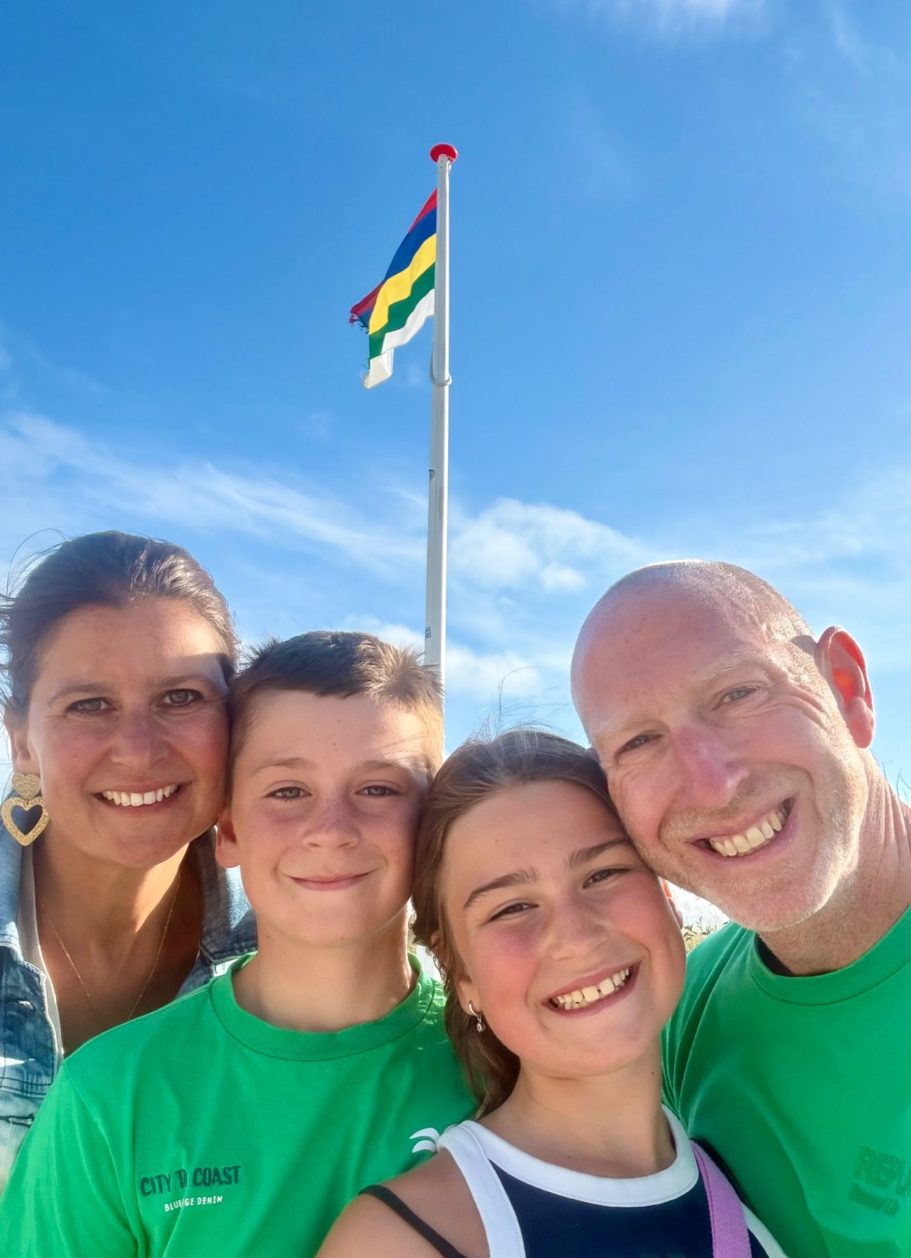 Gezinsportret met vier mensen, met lachende gezichten en zonnige achtergrond.