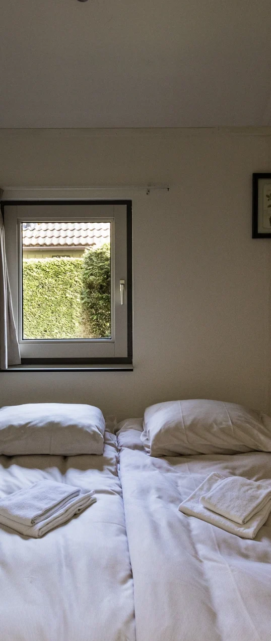 Een slaapkamer met twee bedden en een raam dat uitkijkt op een groene tuin.